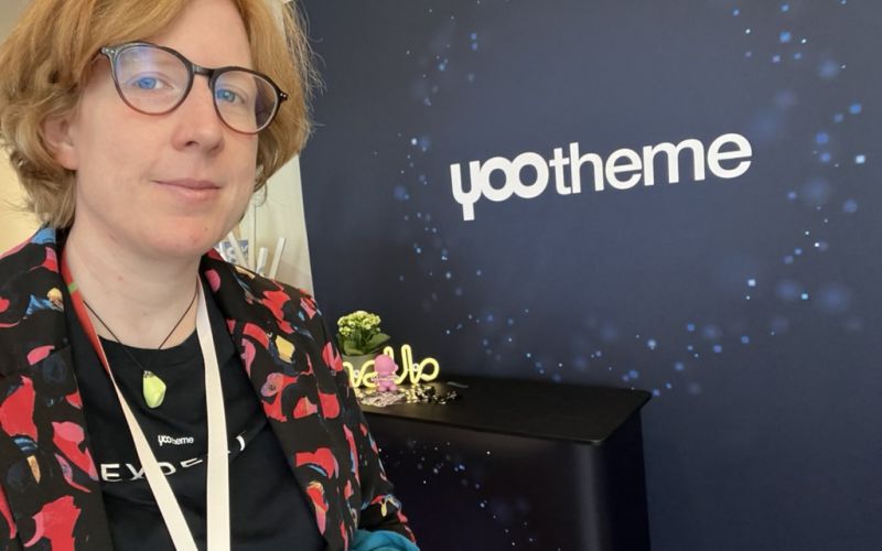 Selfie von Denise vor einem Rollup mit dem YOOtheme-Logo
